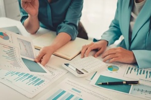 two asian women are reviewing financial transaction documents and calculating expenses with a business idea calculator to increase profits and business