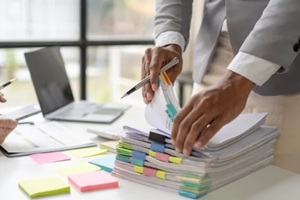 businessman man working in stacks of papers searching for unfinished paperwork information on form check stack on table